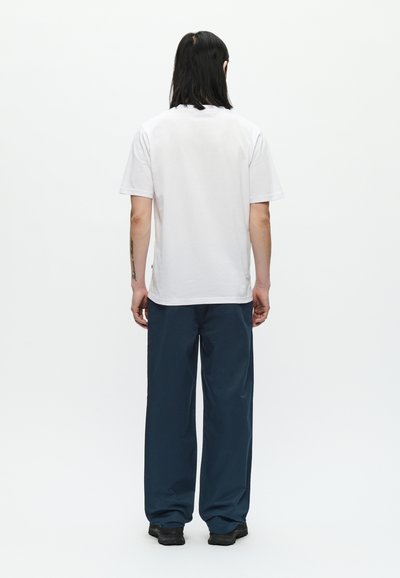 Λευκό βαμβακερό T-shirt με κοντά μανίκια, σε θέα από πίσω. Συνδυασμένο με άνετο, ναυτικό μπλε παντελόνι και μαύρα παπούτσια. Μινιμαλιστικός σχεδιασμός.