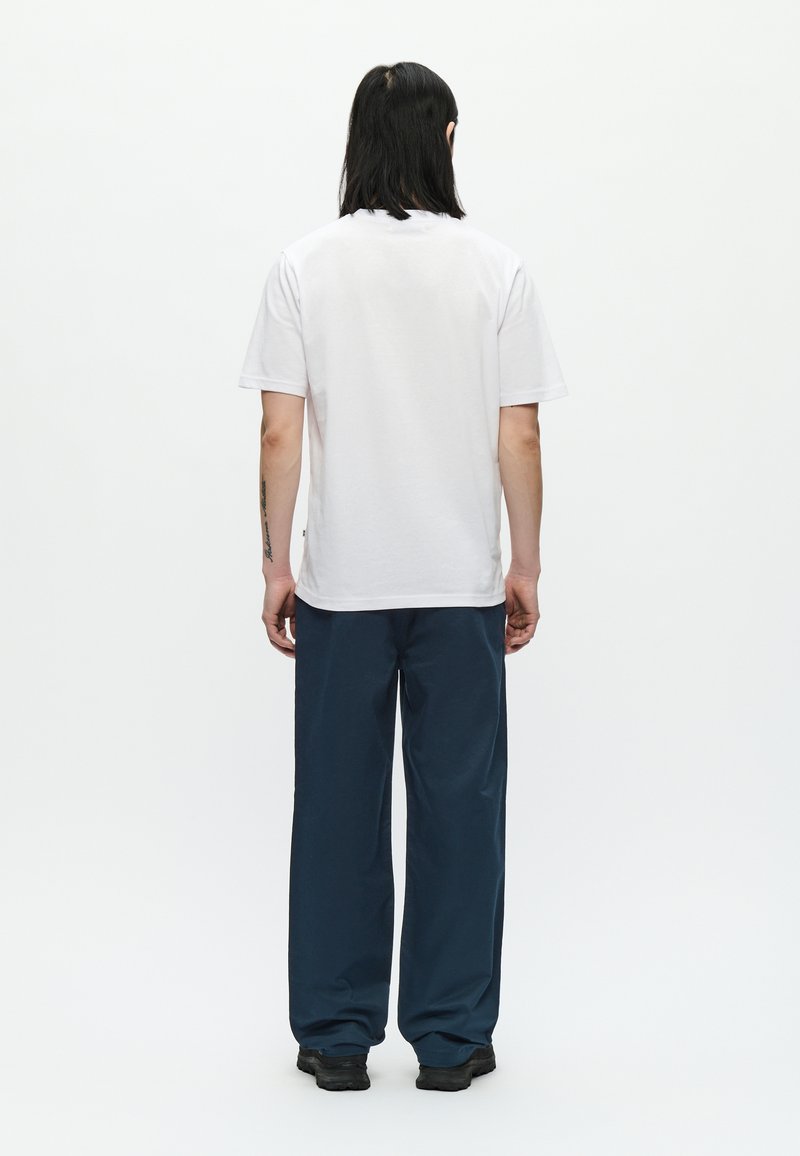 Camiseta blanca de algodón de manga corta vista desde atrás. Combinada con pantalones sueltos azul marino y zapatos negros. Diseño minimalista.