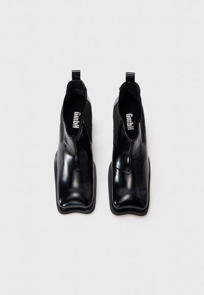 Black ankle boots with glossy patent finish, elastic side panels, pull tabs, and squared toe design. Sturdy rubber sole with a minimal texture.