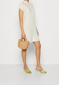 Gestreiftes Hemdblusenkleid in Pastellfarben, kombiniert mit grünen Riemchensandalen und einer tanfarbenen geflochtenen Handtasche. Glatter Stoff und lässige Passform.