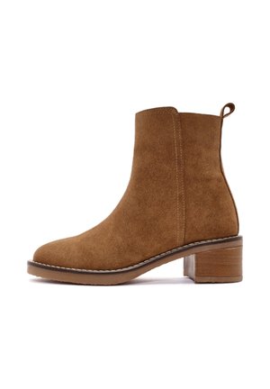 Stivale alla caviglia in suede marrone con punta arrotondata, tacco basso a blocco, cuciture laterali e un manico sul retro per una calzata facile.