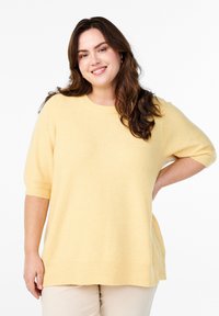 Lys gul, kortærmet strikket sweater med rund halsudskæring og ribbet kant. Blød tekstur, afslappet pasform og slids ved bunden.