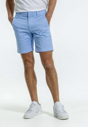 Shorts bleu clair en mélange de coton, dotés de deux poches latérales et d'une coupe classique avec une conception à jambe droite. Portés avec des baskets blanches.