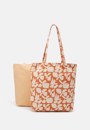 Deux sacs fourre-tout, un beige uni et un orange avec des motifs abstraits de papillons blancs, côte à côte sur un fond blanc.