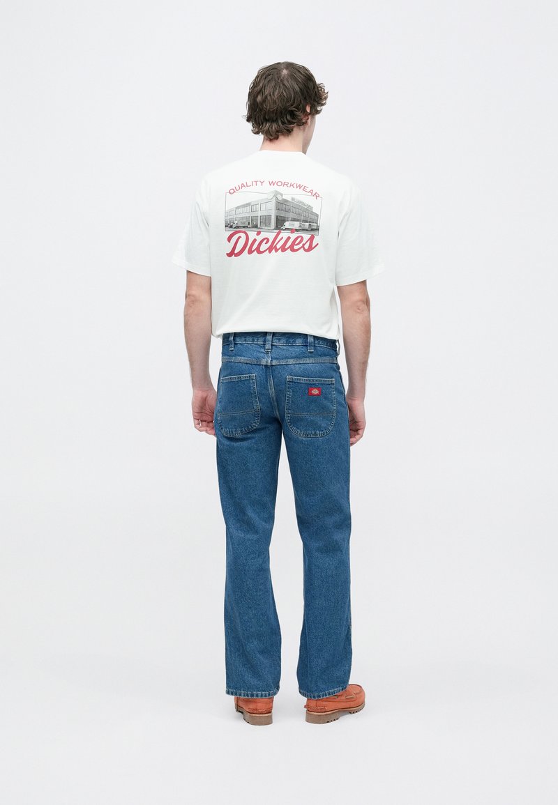 White cotton t-shirt with a graphic print on the back, paired with blue denim jeans and brown shoes. Simple, relaxed fit overall.