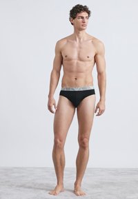 Fekete pamut alsónadrág szürke elasztikus, logóval díszített derékpánttal. Egyszerű kialakítású, egyszínű, sima textúrájú, testhez álló fazon.