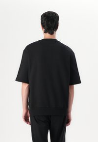 Sweatshirt noir surdimensionné à col rond et à manches courtes, fabriqué dans un tissu doux, présentant un col et un ourlet côtelés. Design simple.