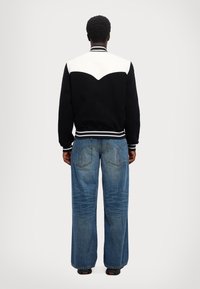 Zwart-wit varsityjack met een gebogen witte schouderpartij; gecombineerd met wijde blauwe denim jeans met stiksels op de achterzak.