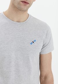 T-shirt din bumbac gri cu un mic design brodat în formă de satelit, în culori albastre și roșii. Mâneci scurte și decolteu rotund. Textură moale.