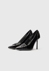 Cizme stiletto negre, lucioase, cu vârf ascuțit, decorate cu curele cu studs pe partea din față și detaliu de marcă pe toc.