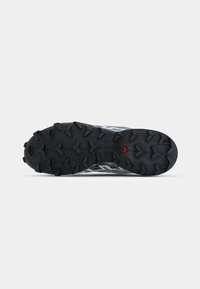 Semelle de chaussure de sport noire avec des crampons proéminents pour une meilleure traction ; accents gris et design texturé ; présente un détail triangulaire rouge.