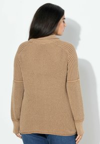 Beżowy sweter dziany z wysokim kołnierzem, prążkowanymi akcentami na ramionach i mankietach, teksturowanym korpusem, luźnym krojem i dłuższym tyłem.