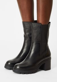 Czarne skórzane botki za kostkę z elastycznymi panelami bocznymi, masywną podeszwą i teksturowaną gumową podeszwą, charakteryzujące się gładkim wykończeniem i zaokrąglonym noskiem.