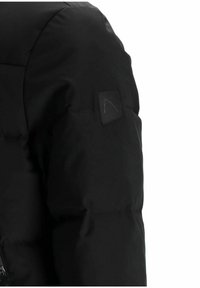 Primer plano de la manga de una chaqueta acolchada negra con un pequeño parche cuadrado que muestra un logo lineal minimalista en la parte superior del brazo.