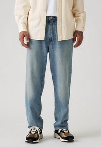 Lichtblauwe denim jeans met een losse pasvorm, met een rechte pijpdesign en subtiele vervaging. Gecombineerd met zwarte en beige sneakers.
