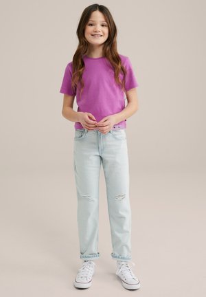T-shirt di cotone viola con una piccola stampa frontale, abbinata a jeans strappati azzurri e sneakers bianche. Design semplice, vestibilità casual.