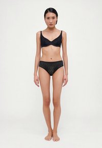 Čierna čipková podprsenka s kosticami a zvlnenými okrajmi. K tomu zodpovedajúce čierne čipkované nohavičky s kvetinovým vzorom a elastickým pásom.