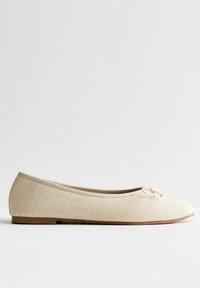 Bailarinas beige con tejido texturizado, punta afilada y un pequeño lazo en la parte delantera. Suela plana y forro interior suave.