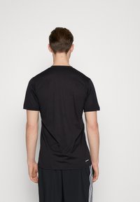 Svart t-shirt med kort ärm och rund hals, tillverkad av mjukt tyg, med en enkel design och en liten logotyp nära fållen.