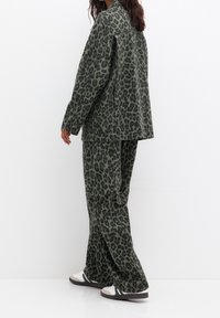 Green leopard print jacket and matching pants made of textured fabric, featuring a relaxed fit and traditional lapel collar.