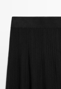 Tissu en tricot côtelé noir avec une large ceinture élastique, montrant la texture et les détails du motif vertical sur un fond blanc.