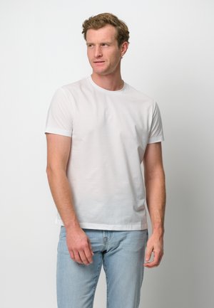 Camiseta blanca de manga corta hecha de tela suave, con cuello redondo, diseño minimalista, combinada con jeans de color azul claro.