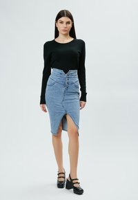 Pull noir ajusté, jupe en denim clair taille haute avec une fente avant, cinq boutons et poches avant. Chaussures plateformes noires avec des lanières.