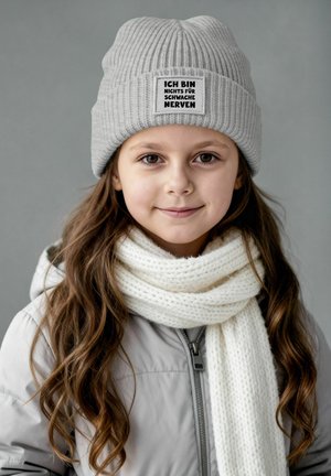 Gray ribbed knit beanie with a patch reading "ICH BIN NICHTS FÜR SCHWACHE NERVEN," paired with a white knitted scarf, under a light gray jacket.