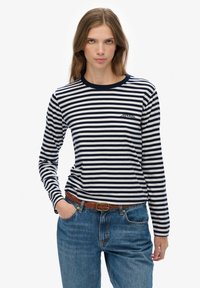 Langærmet stribet skjorte i marineblå og hvid bomuld med rund halsudskæring og et lille logo på venstre bryst. Sammen med blå denim jeans.