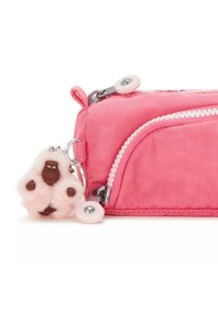 Roze nylon pennenzak met een witte ritssluiting en een ronde roze trekker, voorzien van een fluffy sleutelhangeraccessoire dat op een aap lijkt.