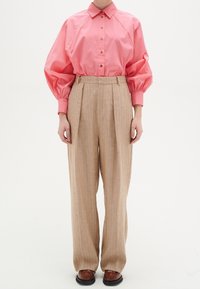 Camicia button-up color corallo con maniche a sbuffo, abbinata a pantaloni beige a righe a vita alta. Completata con scarpe in pelle marrone.