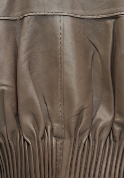 Καφέ δερμάτινο ύφασμα με ορατή ραφή και λεία υφή, που διαθέτει επίπεδη ραφή στην κορυφή και μαζεμένες ενότητες από κάτω.