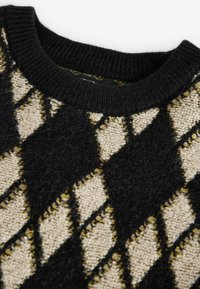Pull en tricot présentant un motif argyle noir, beige et moutarde, une surface texturée et un col rond côtelé noir.