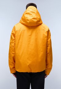 Žlutá kapucová bunda vyrobená z hladkého a lehkého materiálu. Má elastické manžety a stahovací spodní lem; na zadní straně jsou viditelné ploché švy.