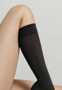 Schwarze Oberschenkelstrümpfe mit transparenter Textur, versehen mit einem gewellten oberen Bund und glatter Oberfläche, vor einem neutralen Hintergrund platziert.