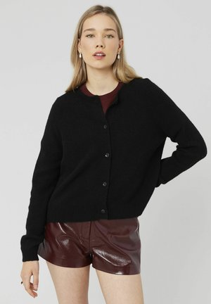 Cardigan noir tricoté avec un col rond, des boutons à l'avant et des poignets côtelés, associé à un short bourgogne brillant. Design simple et texturé.