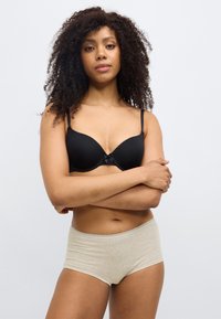 Μαύρο επενδεδυμένο σουτιέν με ρυθμιζόμενους ιμάντες και φιόγκο ως διακοσμητικό στοιχείο· μπεζ σλιπ υψηλής μέσης με απαλό ύφασμα και δαντελένιο τελείωμα κατά μήκος της μέσης.