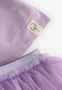 Close-up of a purple fabric sleeve with a smiling face tag and matching lavender tulle skirt with a silver glitter waistband.