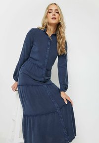 Lång marinblå knappradad klänning med långa ärmar, samlad midja och volangkjol. Tillverkad av mjukt tyg med en slät textur.