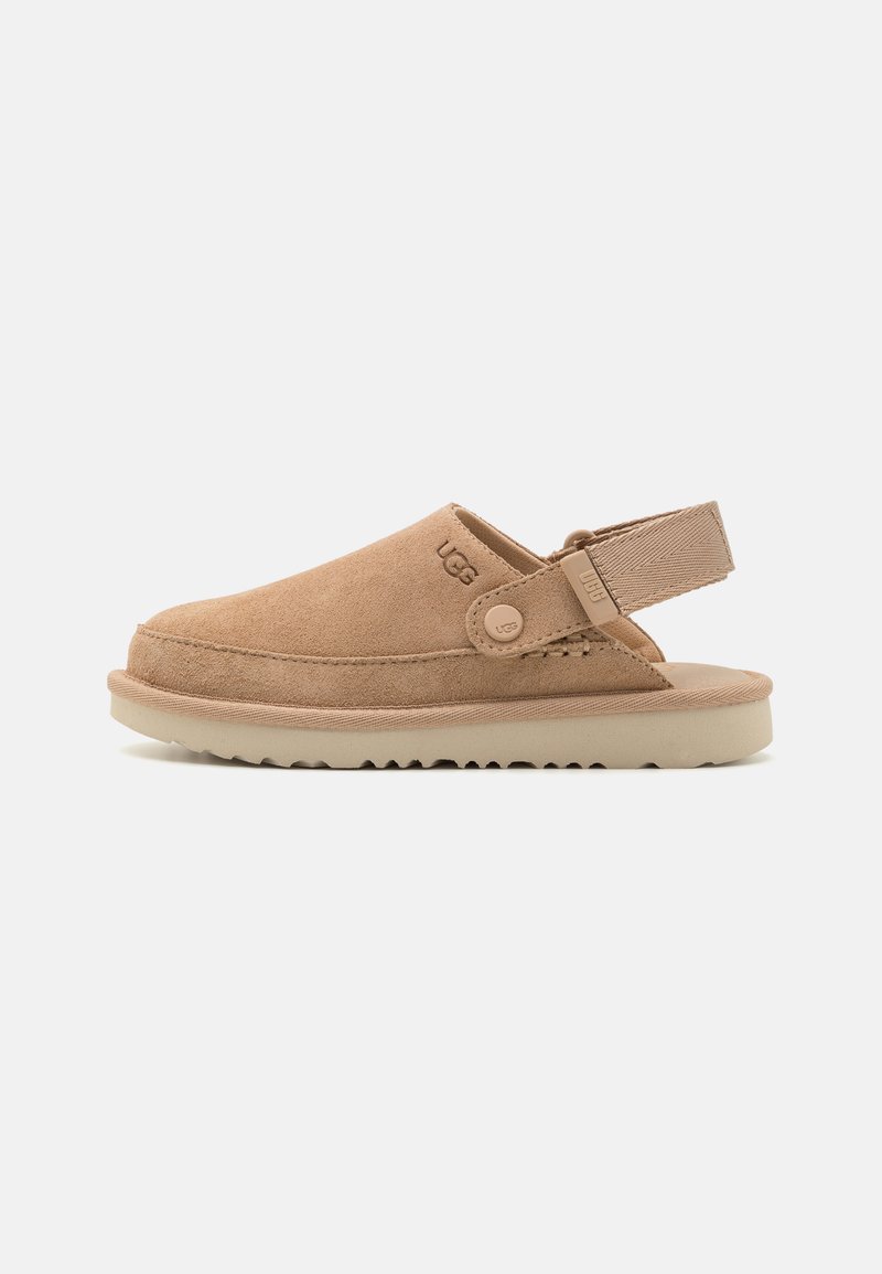 Beige mockasinsandaler med rund tå, bakrem och ett strukturerat gummisul. Har en präglad logotyp på sidan.