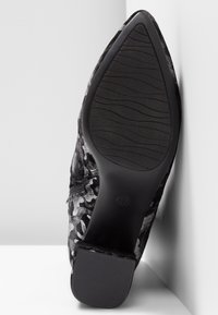 Chaussure noire à bout pointu avec un tissu texturé présentant un motif abstrait blanc. La semelle est en caoutchouc avec une surface antidérapante à motifs pour une meilleure traction.