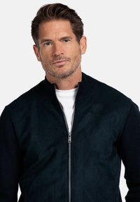 Marineblauwe bomberjack met een suède voorkant, gebreide mouwen en een ritssluiting. Soepele textuur met een klassiek ontwerp en staande kraag.