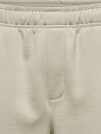 Gros plan sur une ceinture élastique beige sur un pantalon en tissu doux montrant la couture centrale et les détails de la couture.