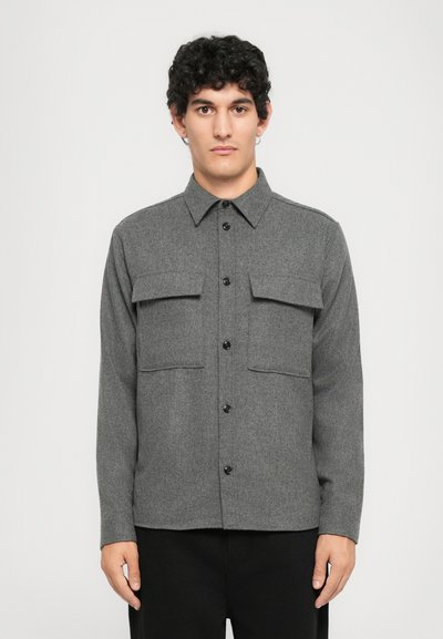 Camisa gris de botones en tejido texturizado con dos bolsillos en el pecho, botones negros y cuello clásico. Mangas largas, diseño de corte recto.