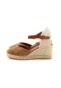 Espadrilles in suede marrone con zeppa in paglia beige intrecciata, cinturino alla caviglia marrone e dettagli in corda naturale. Punta arrotondata e lati aperti.