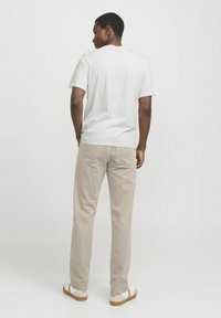 Hvid kortærmet T-shirt, beige lige ben bukser, lys tekstur, med synlige baglommer, parret med hvide sko med brune såler.