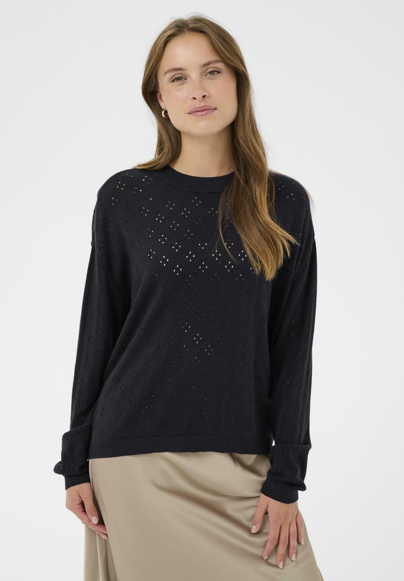 Un pull en tricot noir avec une coupe ample, un col rond et de subtils motifs en losange découpés partout, associé à une jupe en satin beige.