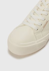 Baskets blanches en cuir texturé avec un bout arrondi, lacets plats et une semelle en caoutchouc avec une surface texturée. Accents en marron clair.