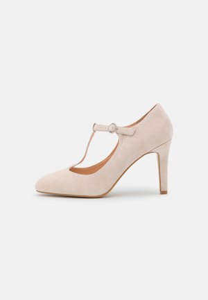 Beiger Wildleder High-Heel mit T-Riemen, runder Spitze und Schnallenverschluss auf einem schlichten hellen Hintergrund.