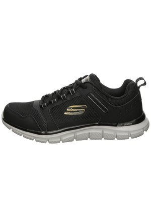 Zapatilla deportiva negra con parte superior de malla, diseño con cordones, acentos metálicos y suela acolchada con ranuras flexibles para tracción.